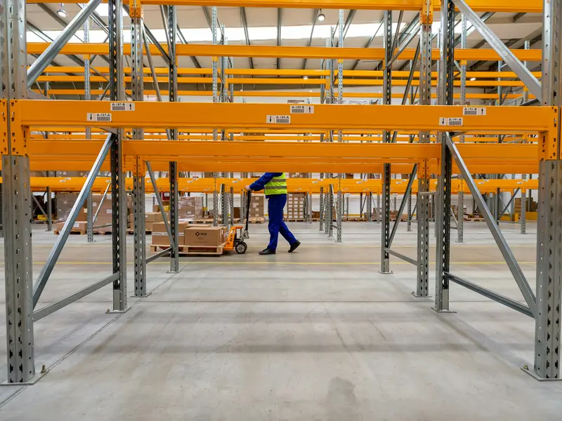 Distribution warehouse with orange pallet racking and a worker moving a pallet jack across the floor