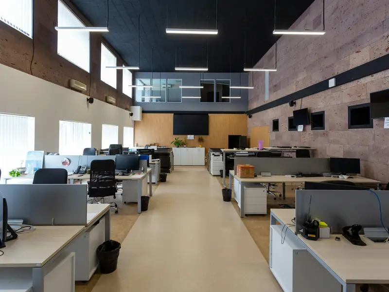 Open-plan office with rows of desks and monitors beneath suspended linear light fixtures