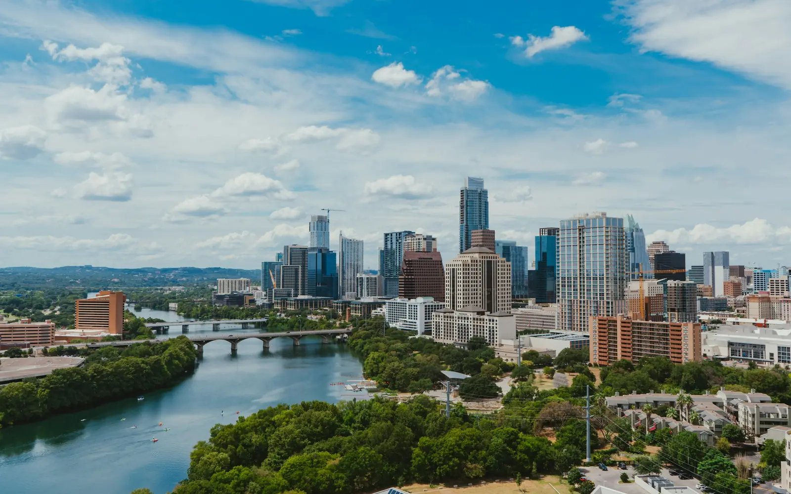 Downtown Austin skyline beside Lady Bird Lake on a sunny day with scattered clouds