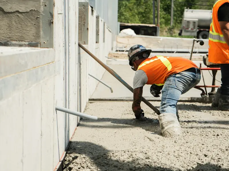 Concrete crew in orange safety vests placing and leveling fresh concrete along a building foundation