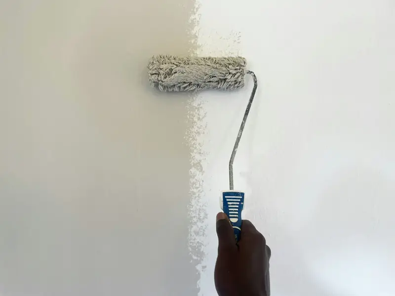 Paint roller applying a fresh coat of white paint across an interior wall